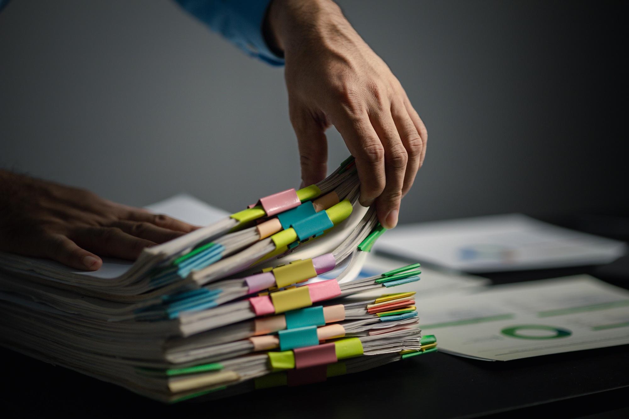 Person with stacks of company financial report papers in office, company employee picking up papers